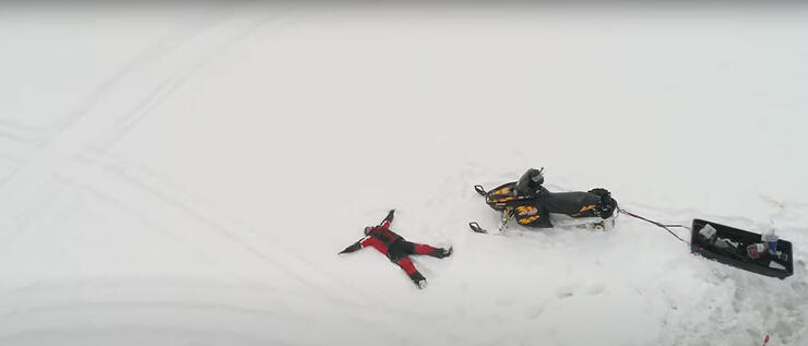 person laying on snow near snowmobile