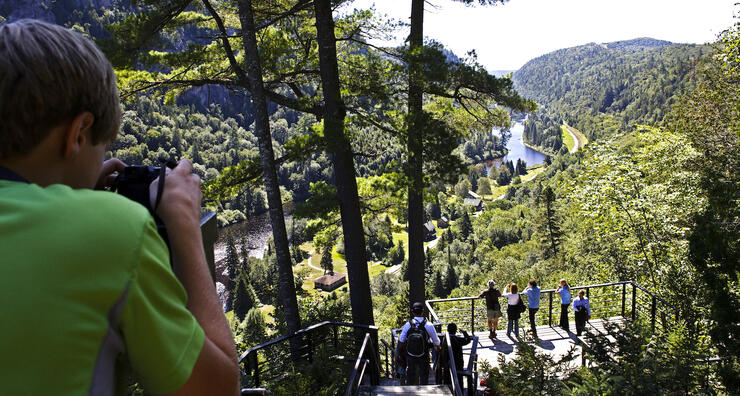 Young boy taking photo of people standing on a platform overlooking Agawa Canyon