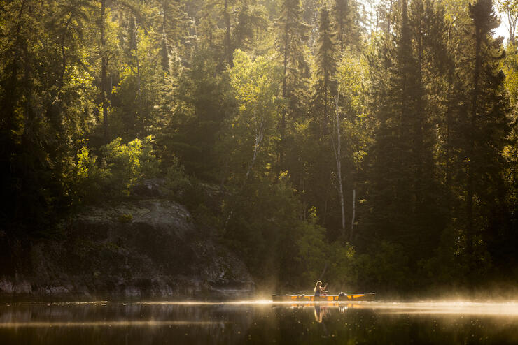 Woman in yellow canoe paddling with mist rising from water.