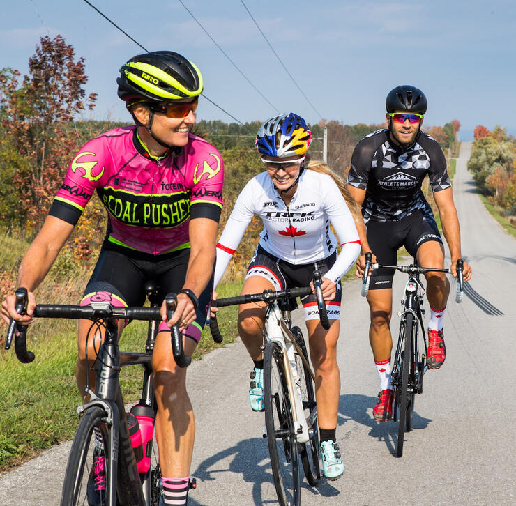 Three friends cycling on paved road in countryside.
