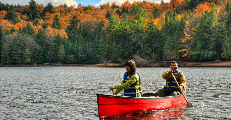 Two people paddling a red canoe in front of a forest of coloured leaves.