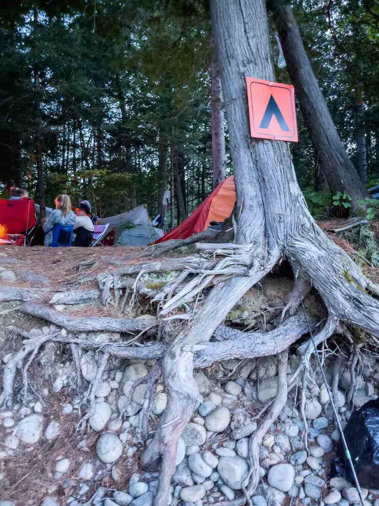 Orange campsite sign with group sitting in lawn chairs around fire in background.