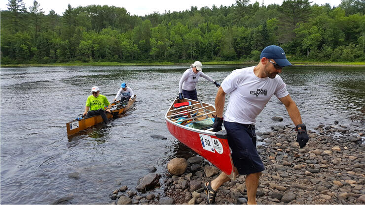 People carrying red canoeing out of water on pebble beach
