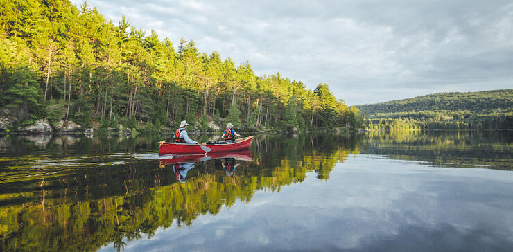 two people paddling a red canoe on a calm lake 
