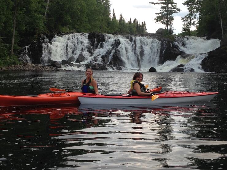 Two people in sea kayaks with waterfall in background