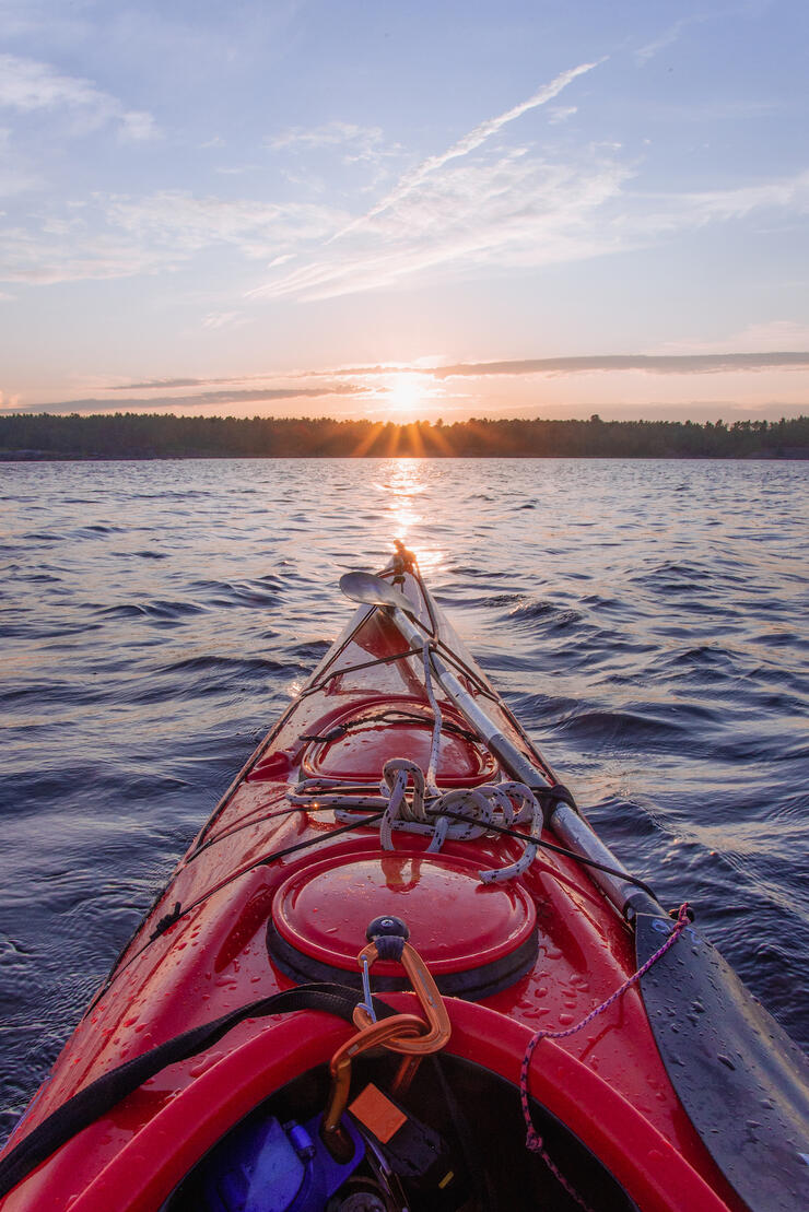 View from kayak across the water as sun sets behind trees