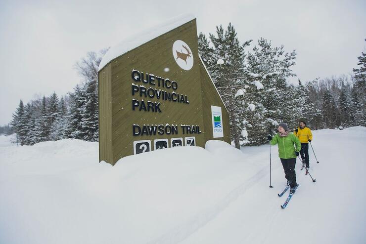 Two people cross country skiing in front of Quetico Provincial Park sign