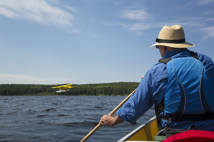 Person at front of canoe watching float plane take off.