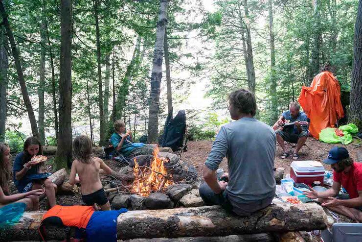 People sitting around campfire in the woods.