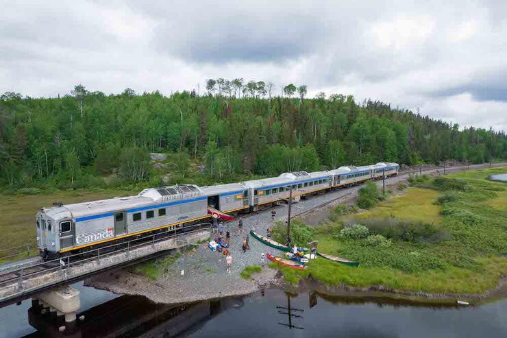 Canoes unloading from a train next to the water.