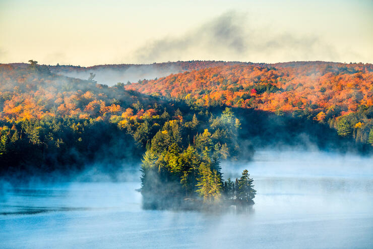 Island on a lake as mist rises up and fall colours line the trees