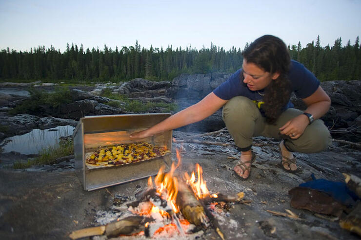 Woman kneels beside reflector oven