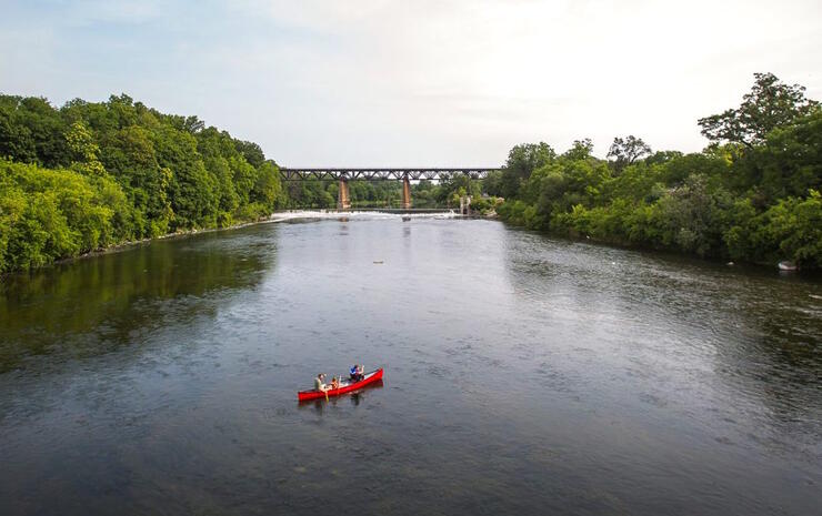 Red canoe on river with train bridge in distance.