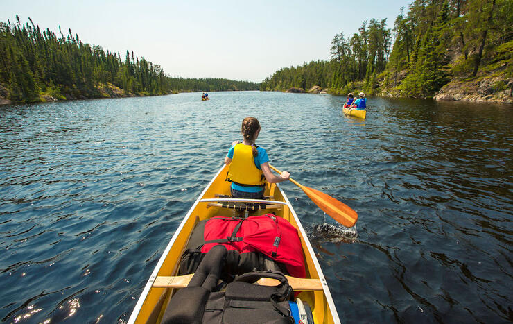 View from stern of canoe with young girl in stern and other canoes in front.