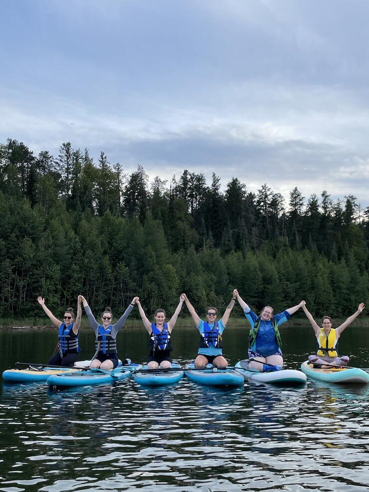 Group of people sitting on paddleboards holding hands in the air