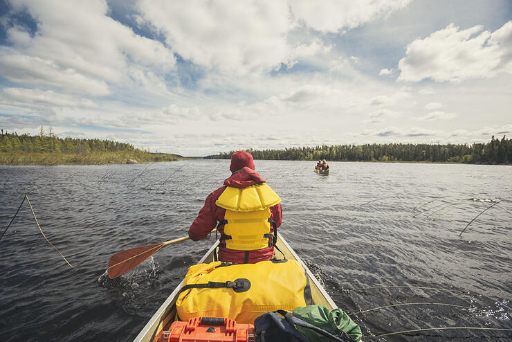 Person with red coat and yellow PFD paddling a canoe on a lake