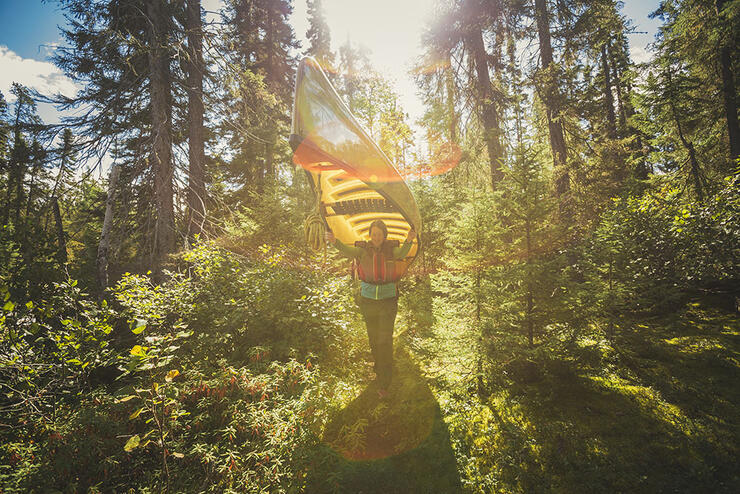 Woman crying a canoe over her head walking through the forest