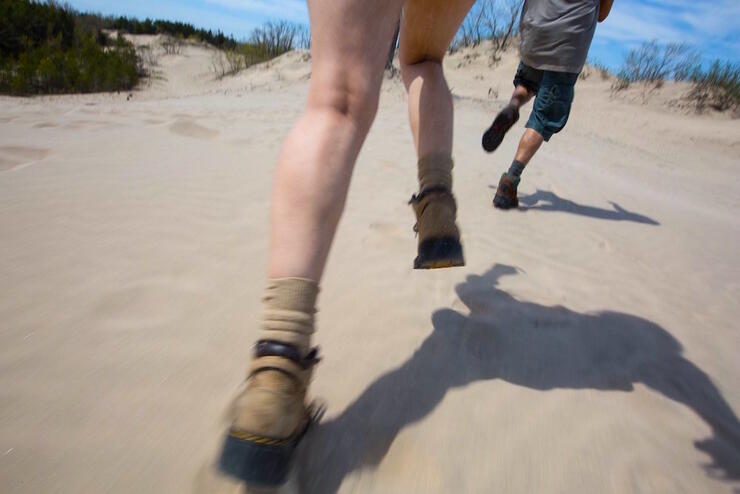 Two people in hiking boots running on sand.