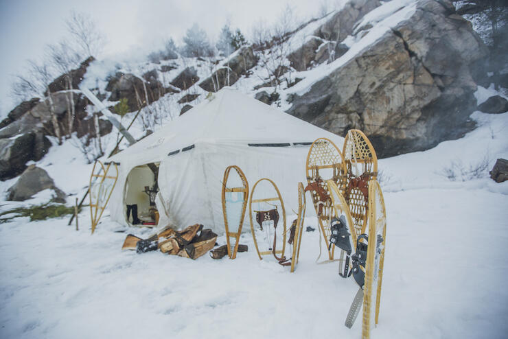 Traditional heated wall canvas tent in snow with snowshoes.