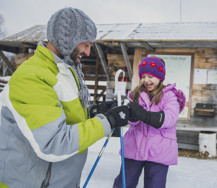 Man and young girl laughing while putting on mittens