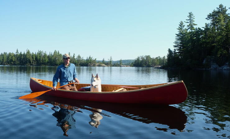 Man paddling a red canoe with a dog sitting in it.
