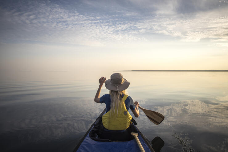 Back of woman paddling on large lake.