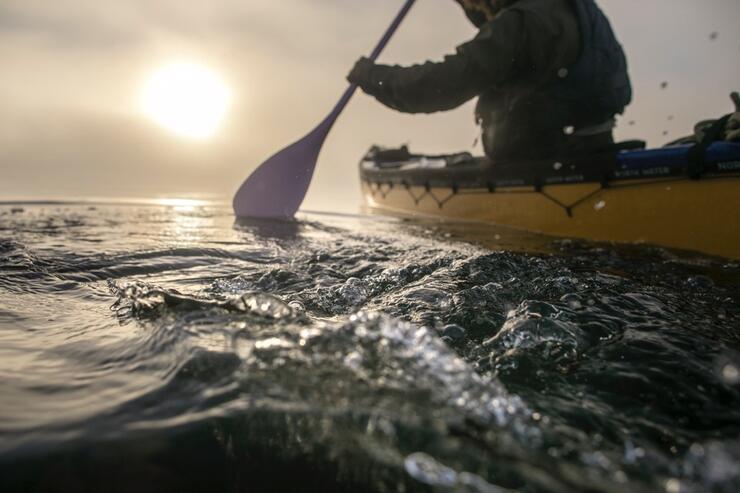 Person with paddle in yellow canoe with water movement in foreground
