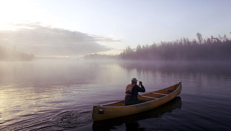 Single man paddling a canoe in early morning mist. 