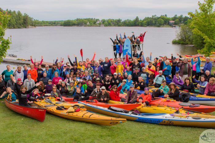 Large group of women in front of lake with kayaks and SUP