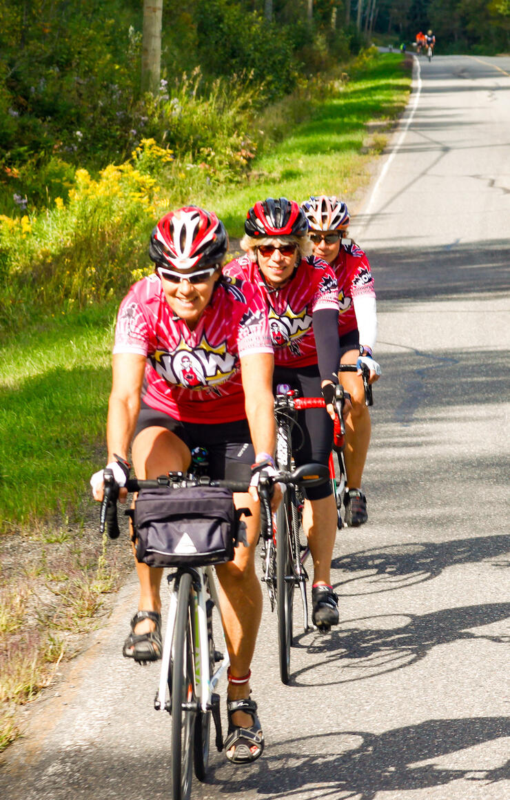 Three women cyclists dressed in colourful spandex riding in single file on road