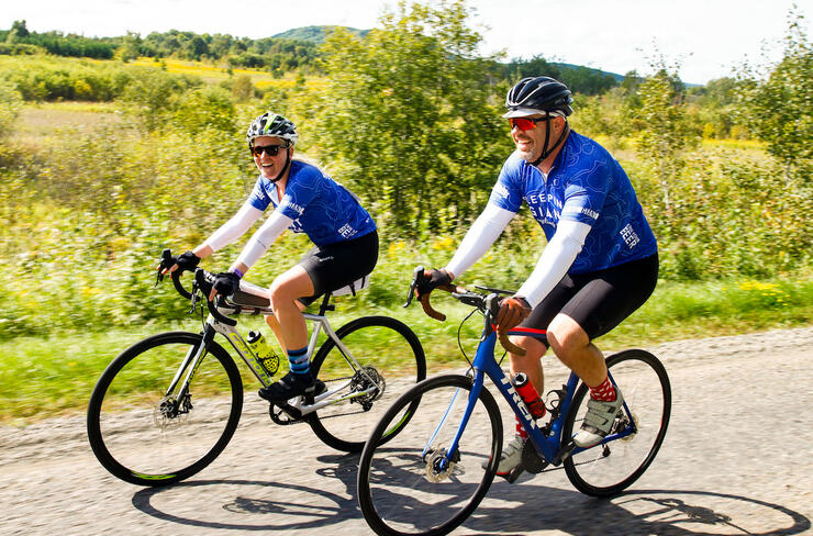two cyclists riding on dirt road with fields in background