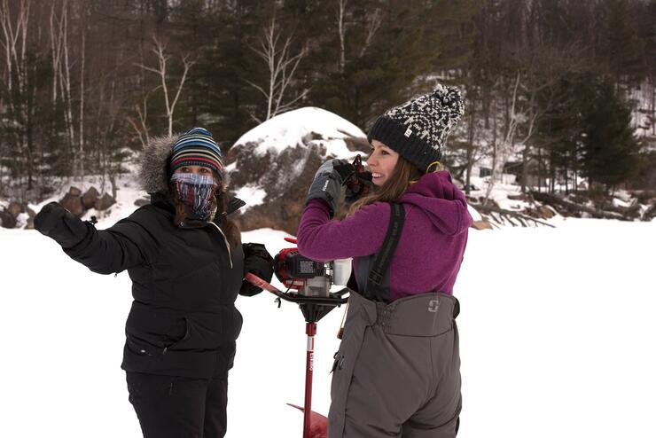 woman anglers drilling ice hole with auger