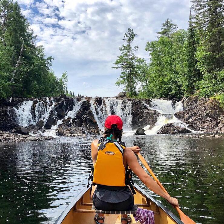 View from back of canoe paddling towards waterfall.