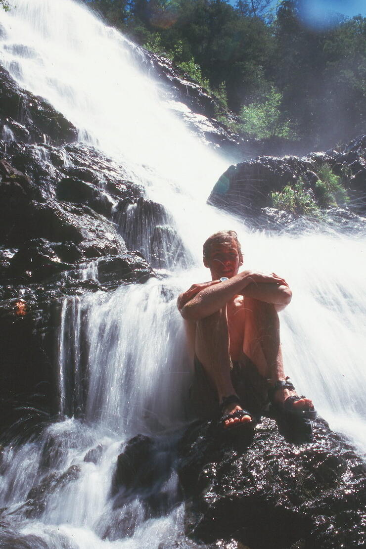 Man sitting on rock at bottom of waterfalls